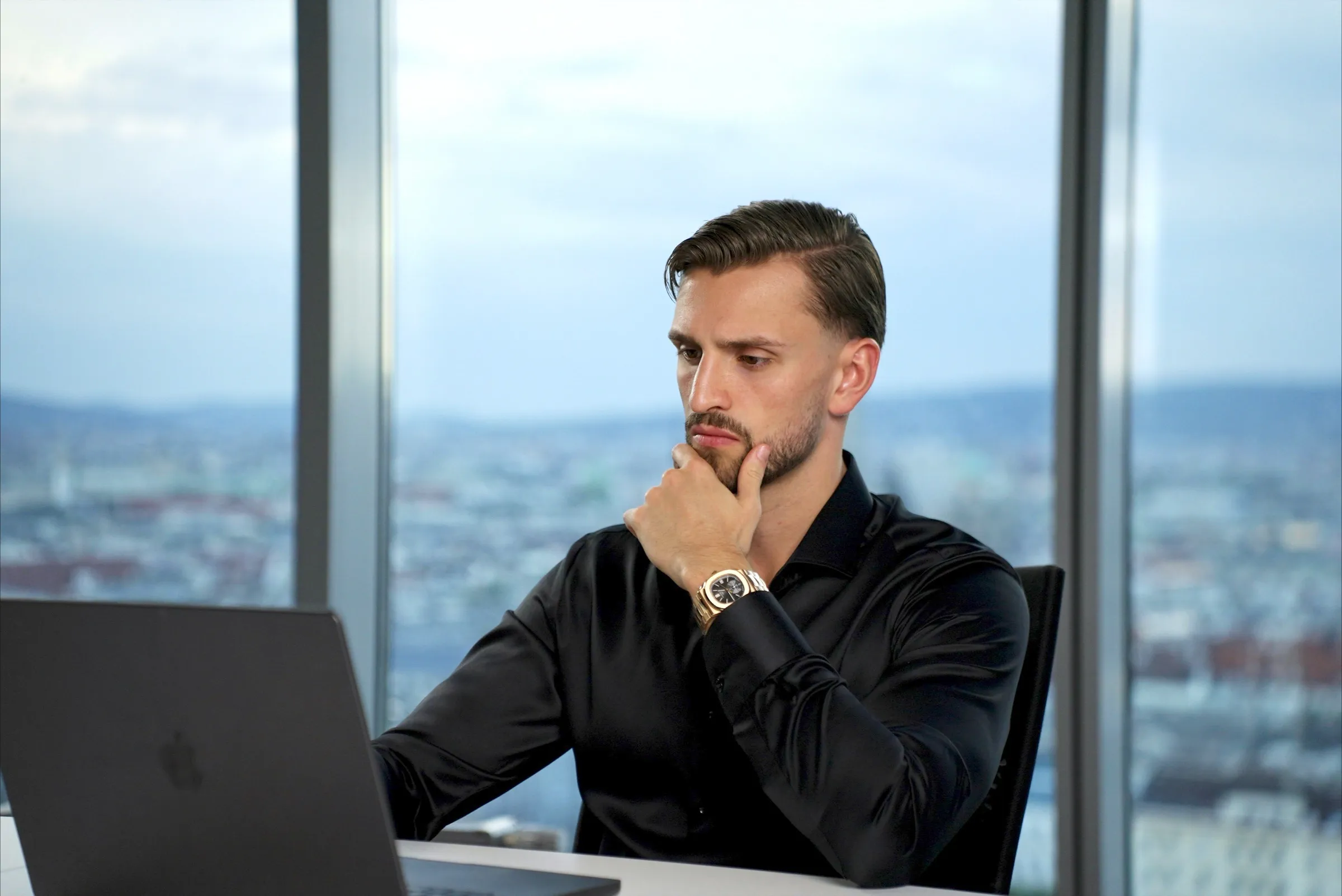 Kilian Kropiunik denkt am Laptop vor einem Fenster mit Blick über die Stadt nach